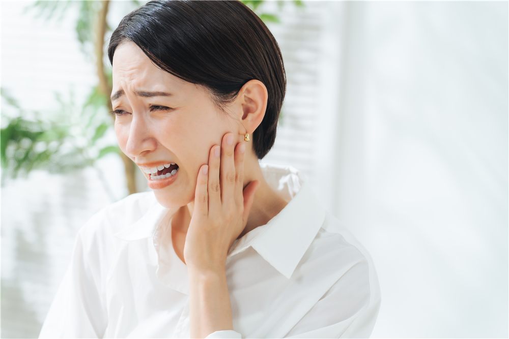 奥歯のあたりを押さえて痛がる女性